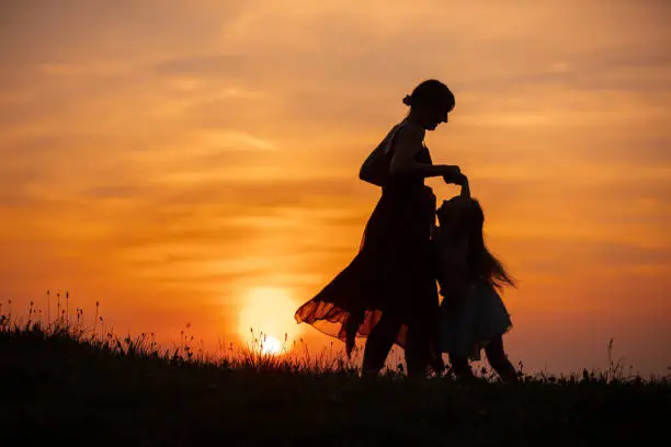Photo of Mother and daughter playing in meadow during sunset