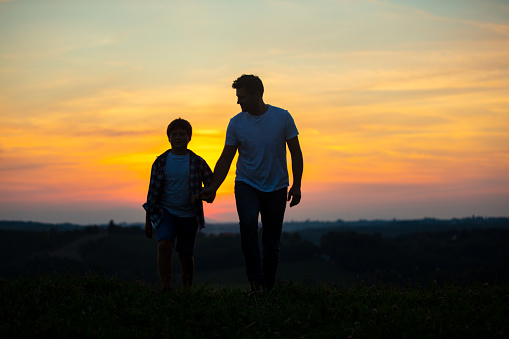 Silhouette of father and son walking on grass field during sunset