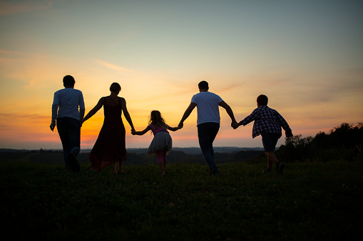 Family holding hands and walking together on grass field during sunset