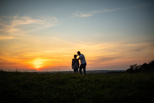 Silhouette of father and son admiring view from grass field during sunset