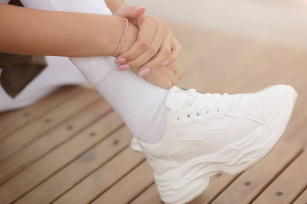 A sporty girl sits on a bench and hugs her leg. Shoe close-up. Break between workouts. stock photo