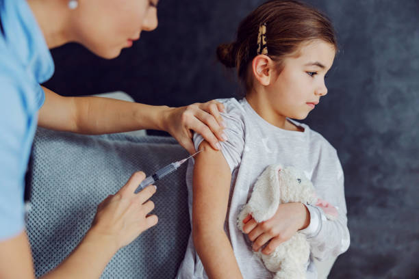 istock Scared little girl sitting on sofa and getting vaccine. 1297397636