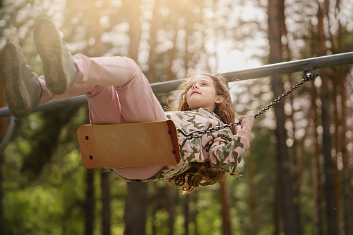 The girl is swinging in the spring park. Happy childhood concept.