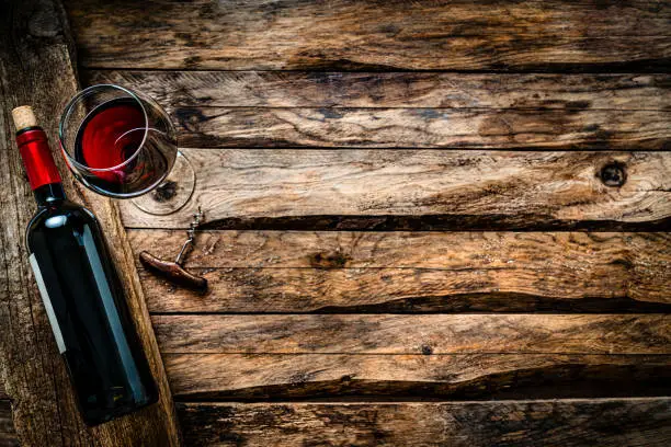 Photo of Red wineglass and bottle shot from above on rustic wooden table. Copy space