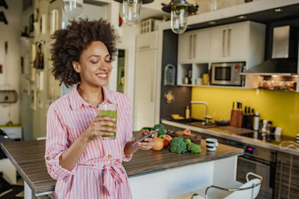 istock Woman is using mobile phone in the kitchen and holding a healthy drink 1297402678