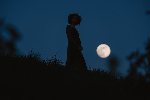 Beautiful silhouette of a young woman against a background of the night sky with a full moon