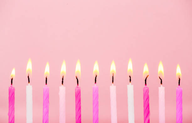 istock Various pink color birthday cake candles burning in line on pastel pink background, studio shot, lot of copy space for greetings. Side view. 1297407918