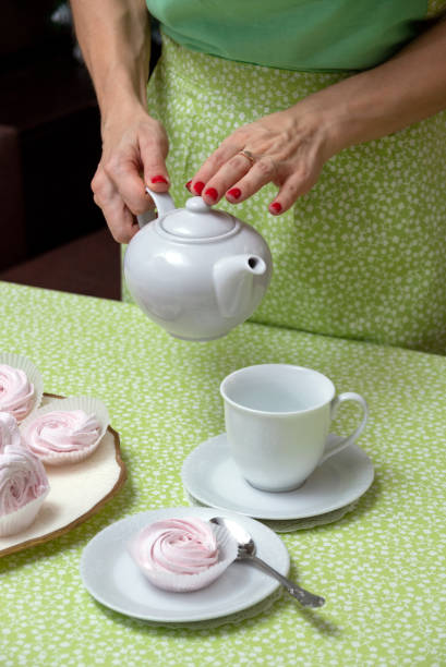 istock Red-manicured hands hold a white teapot before pouring tea into a cup. Selective focus. 1297407978