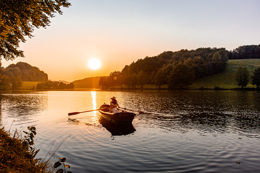 Woman in a wooden boat rowing across the lake during sunset