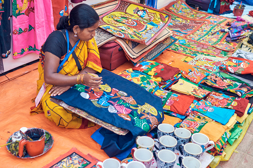 Saras Mela, Kolkata, 03/01/2020: A rural craft-woman belonging to West Bengal rural development communities, painting tribal fish motifs on ladies kurtas, ceramic cups etc. which are there for sale.