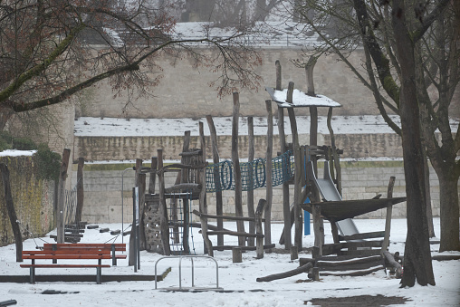 Snow covered deserted children´s playground with slide and climbing towers surrounded by stone buildings and walls in the old town of Regensburg in winter