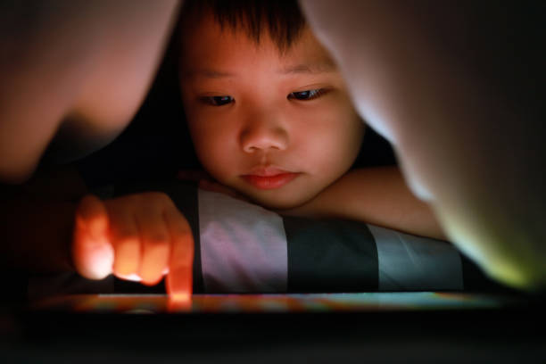 istock Little Asian boy hiding in the blanket on bed and playing digital tablet. 1297414827