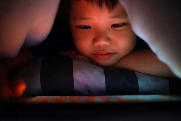 istock Little Asian boy hiding in the blanket on bed and playing digital tablet. 1297414861