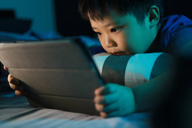 istock Little Asian boy lying on the bed at night and playing digital tablet. 1297414898