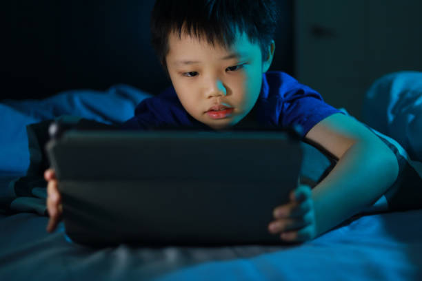 istock Little Asian boy lying on the bed at night and playing digital tablet. 1297414905