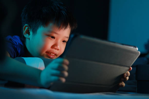 istock Little Asian boy lying on the bed at night and playing digital tablet. 1297414940