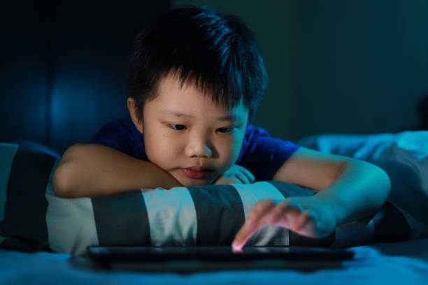 istock Little Asian boy lying on the bed at night and playing digital tablet. 1297414948