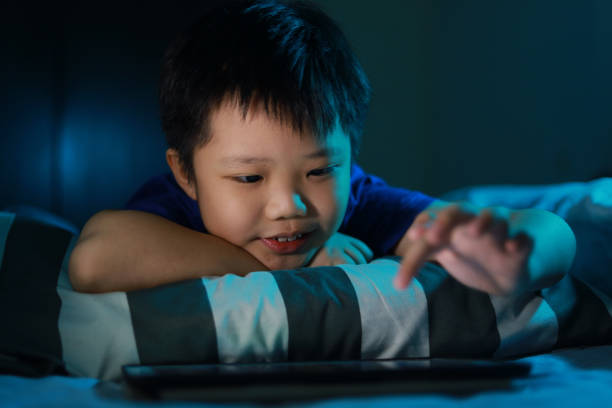 istock Little Asian boy lying on the bed at night and playing digital tablet. 1297414950