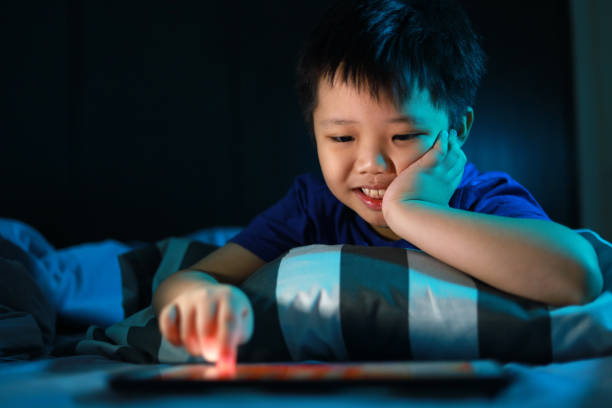 istock Little Asian boy lying on the bed at night and playing digital tablet. 1297414992