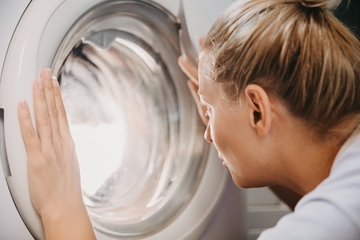 Curious young woman looking into washing machine