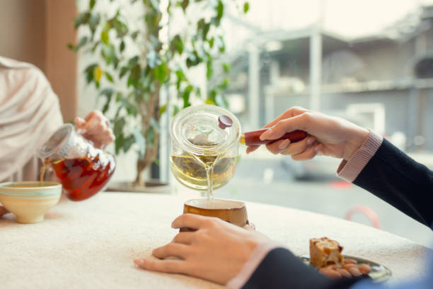 Close up female hands pouring tea in cup at restaurant or cafe, daily lifestyle