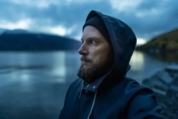 Bearded fisherman portrait: with raincoat by a fjord at night