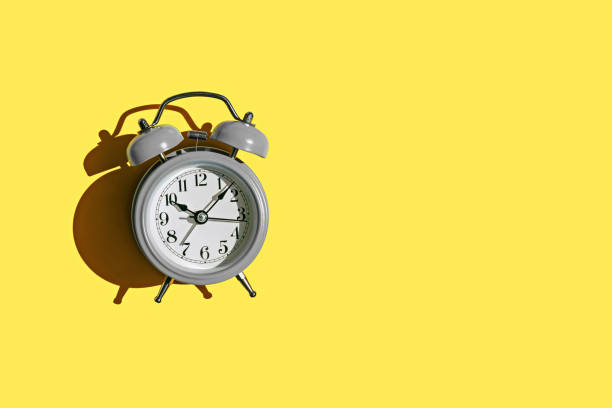 istock Grey alarm clock on yellow background with copy space. Color 2021. 1297417580