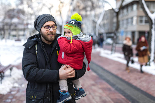 Cute little son sitting on his father's shoulders. Happy dad and toddler son spending time together outdoors enjoying summer. Happy fatherhood and childhood, family love, togetherness concept.