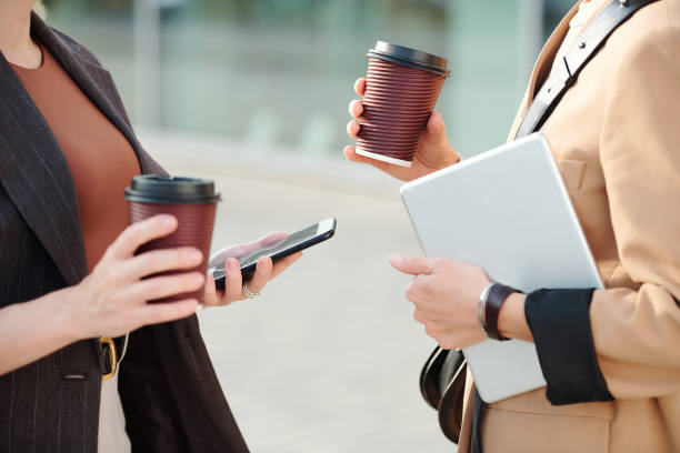 Two young contemporary businesswomen having drinks and using mobile gadgets
