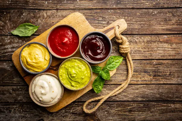 Set of different bowls of various dip sauces on wooden background, top view