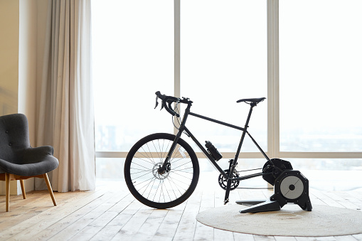Black exercise bicycle or bicycle trainer in room with large windows and chair