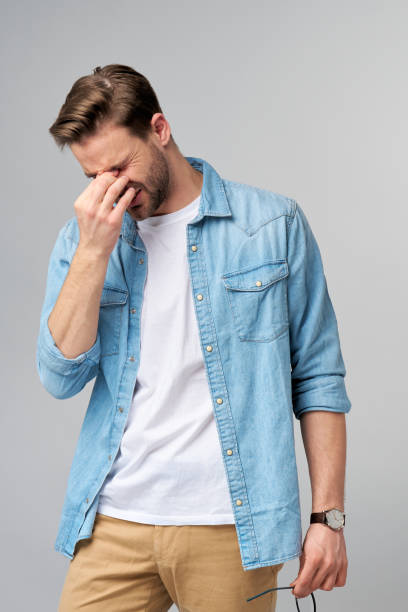istock Frustrated young caucasian man in jeans shirt touching head with hand while standing overg studio grey background 1297420823