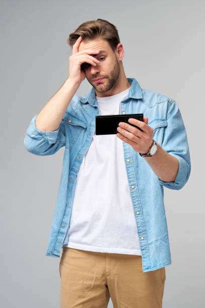 istock Young shocked stressed angry and frustrated man using smartphone over grey background 1297420896