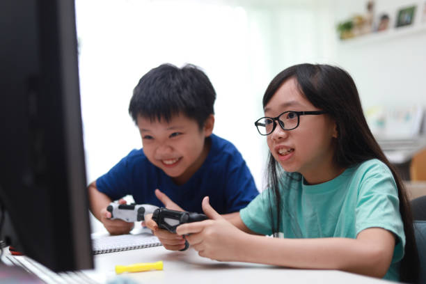 Happy siblings playing video game in living room. Boy and girl in the living room playing video game in front monitor screen together. Soft focus image. handheld video game stock pictures, royalty-free photos & images