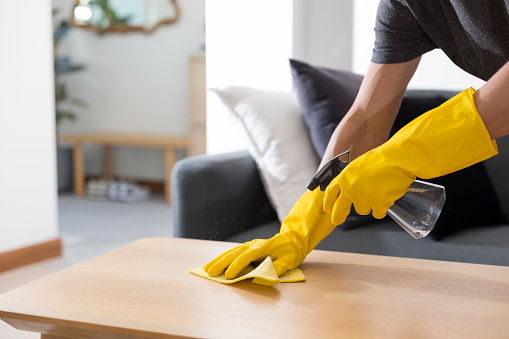 Sanitising surfaces cleaning home table with disinfectant spray with towel and gloves. COVID-19 prevention.