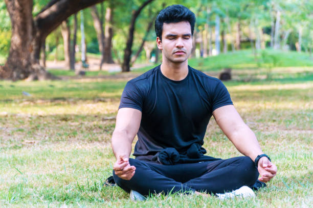 istock Handsome young indian guy practicing yoga in the park Serene yoga man practitioner workout and sitting in lotus pose or asana with closed eyes. Yoga and meditation healthy concept 1297426004