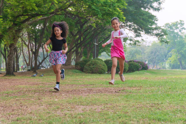 istock Cheerful two little kids having fun while running through grassy field with tree and racing against each other. Cute girl enjoying with her friend run on green meadow in park. Best friends concept. 1297426009