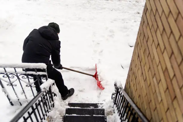 Photo of Senior man shoveling snow from stair case on city street.