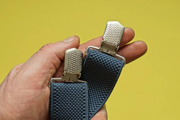 hand holds two blue fabric braces with gray metal snaps on a yellow background