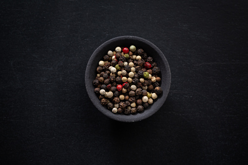 Color whole peppercorns  in small bowl on dark background.