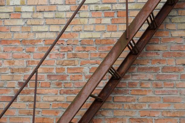 part of brown iron rusty staircase with steps and handrails against a brick wall in the street