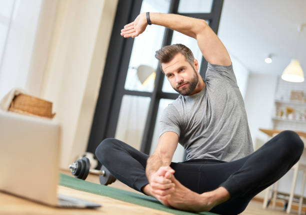 istock Bearded young man using laptop and doing morning gymnastics 1297433150