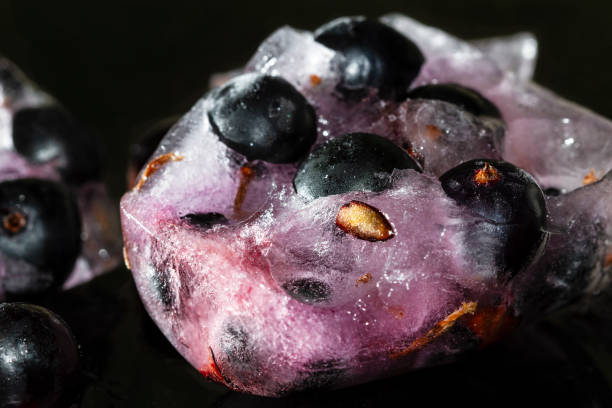 istock Black currant berries frozen in ice with reflection on dark background. Cracked ice. Closeup, selective focus 1297434251