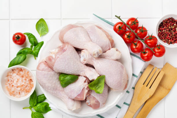 Raw chicken meat, ready for grill or barbeque legs, with tomatoes, herbs and spices on light white kitchen table background. Top view. Raw chicken meat, ready for grill or barbeque legs, with tomatoes, herbs and spices on light white kitchen table background. Top view. ugly soup stock pictures, royalty-free photos & images