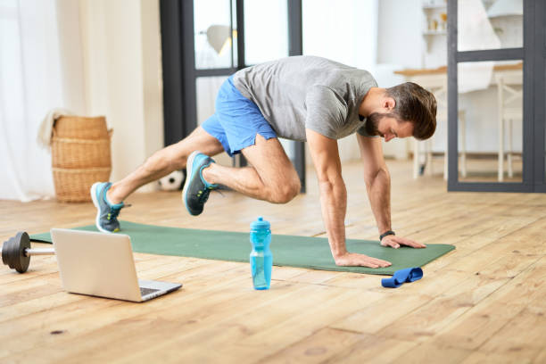 istock Bearded young man using laptop during morning workout at home 1297436373
