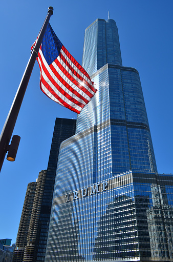 Chicago, IL, USA - March 28, 2015: The Trump International Hotel and Tower, designed by architect Adrian Smith of Skidmore, Owings and Merrill, with an American flag in the foreground.