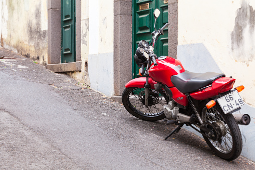 Funchal, Portugal - August 24, 2017: Red Honda CG125 or Honda CG stands parked near old wall on a narrow street, rear view. It is a commuter motorcycle made by Honda of Japan