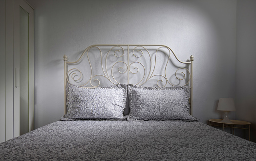 Front view of classic style interior bedroom with double bed, forged headboard, lace bedlinen on white wall background
