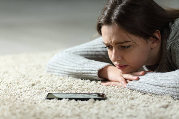 Sad teen waiting for phone message on the floor at home Sad teen waiting for phone message on the floor at home cyberbullying stock pictures, royalty-free photos & images