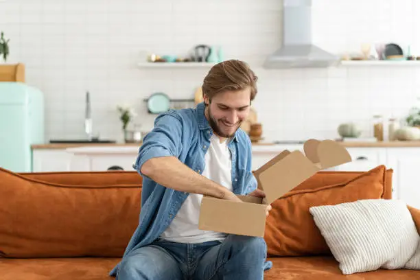 Photo of Happy man customer unpacking cardboard box receive open post mail delivery package